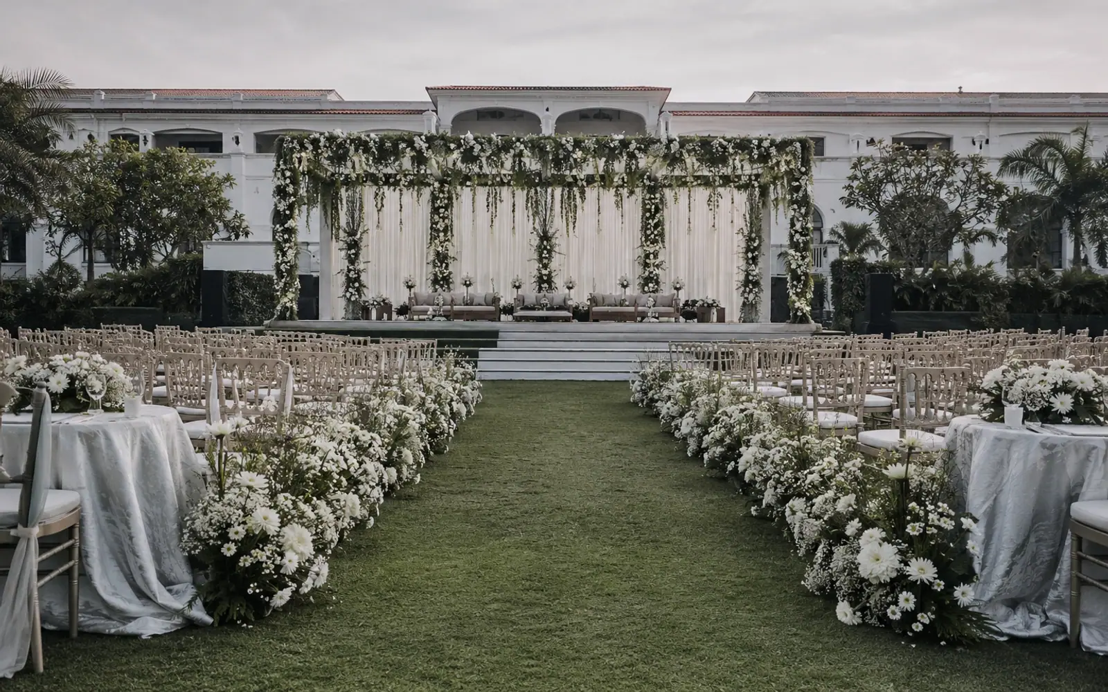 A wedding ceremony set on a lawn: an aisle edged with white gerbera and gypsophila leading to a draped floral stage.